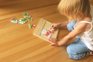 2-3 years old girl kneeling on the floor and solving jigsaw puzzle